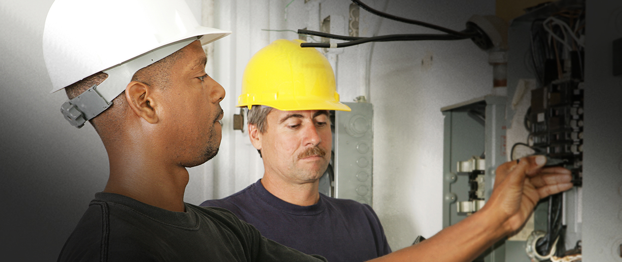Two men in hard hats looking at a wall.